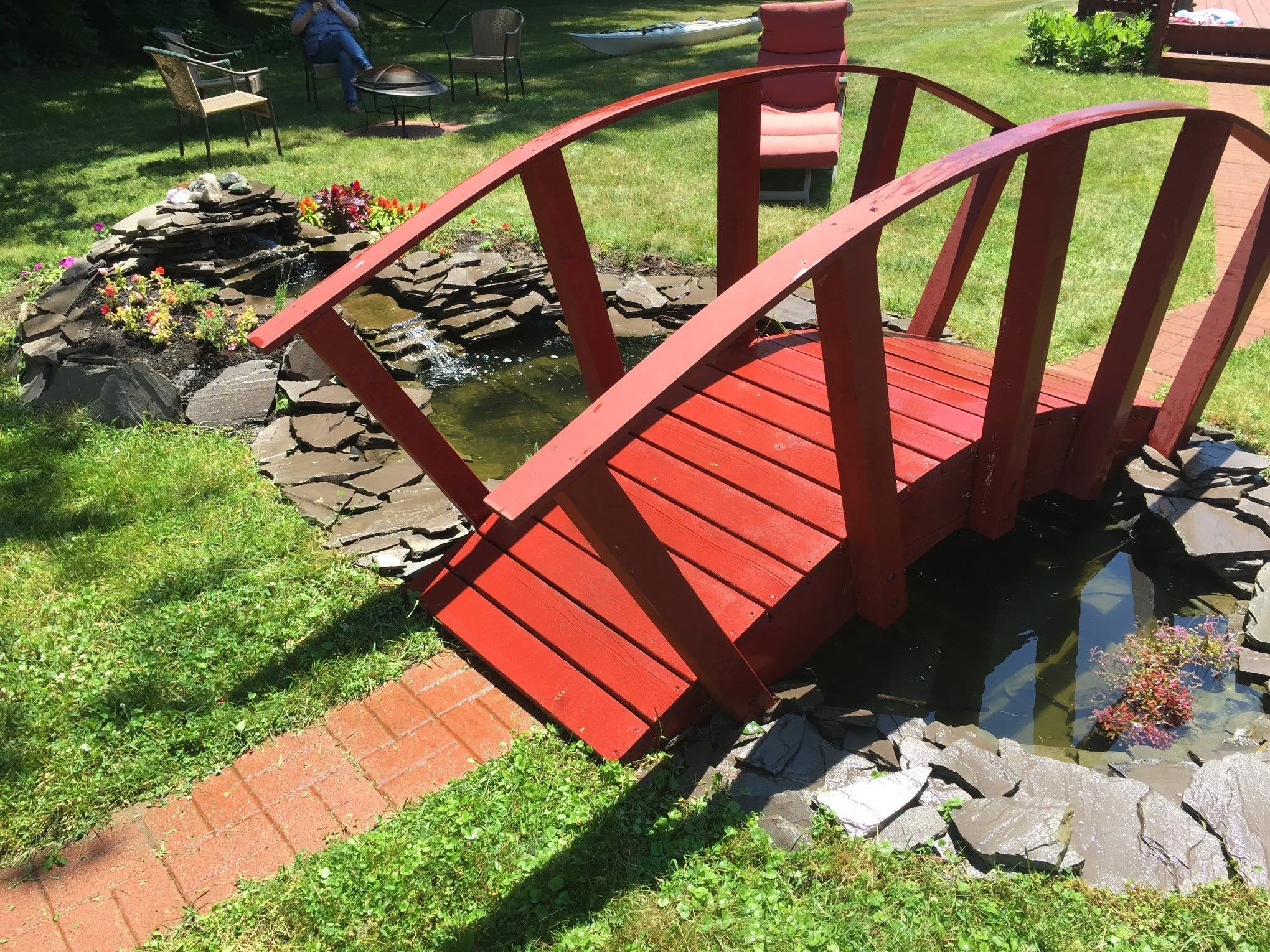 Curved red wood footbridge over a backyard pond
