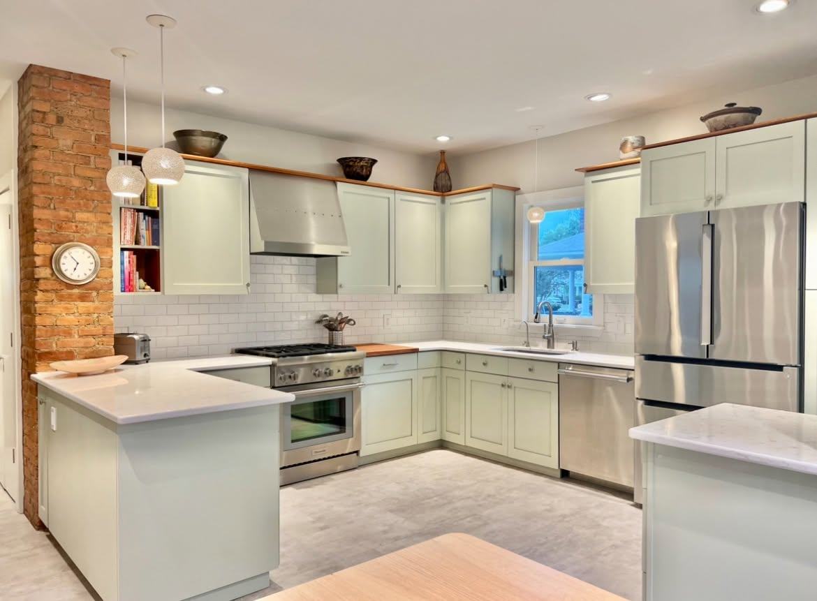 Kitchen with sage green cabinets, white counters, stainless appliances and an exposed brick chimney